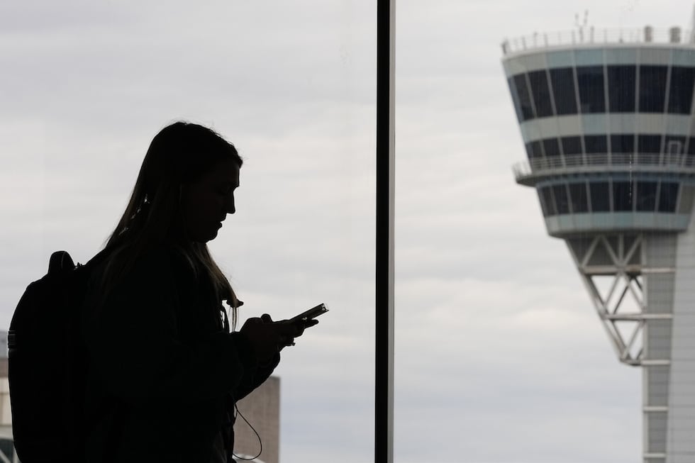 FILE - A traveler with a smartphone walks past an air traffic control tower at Philadelphia...